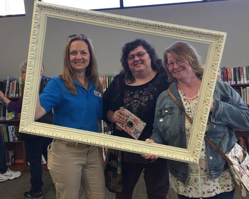 3 IHLS staff members holding a large, empty photo frame